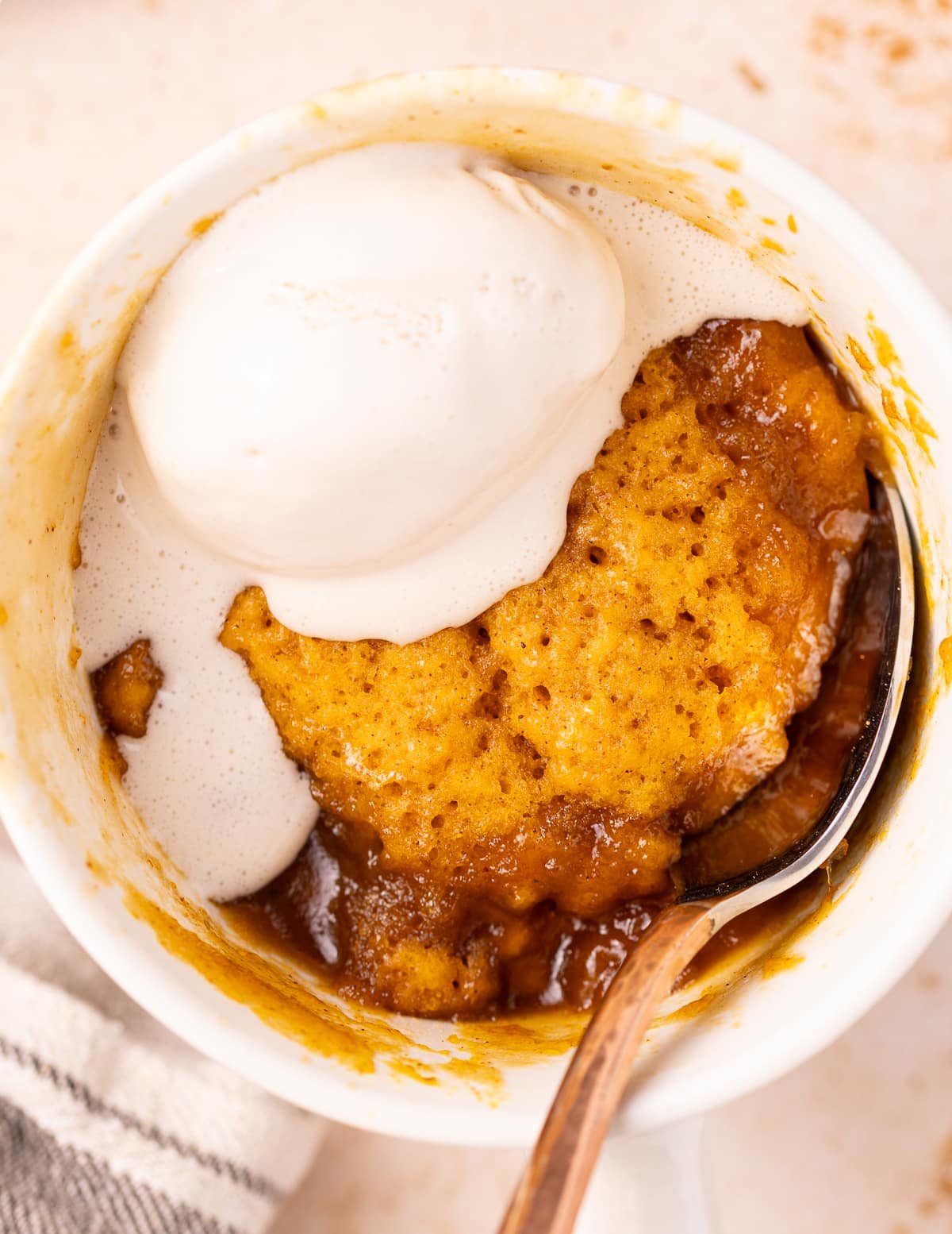 A pumpkin mug cake with bubbly caramel around the edges and a big dollop of white ice cream. 