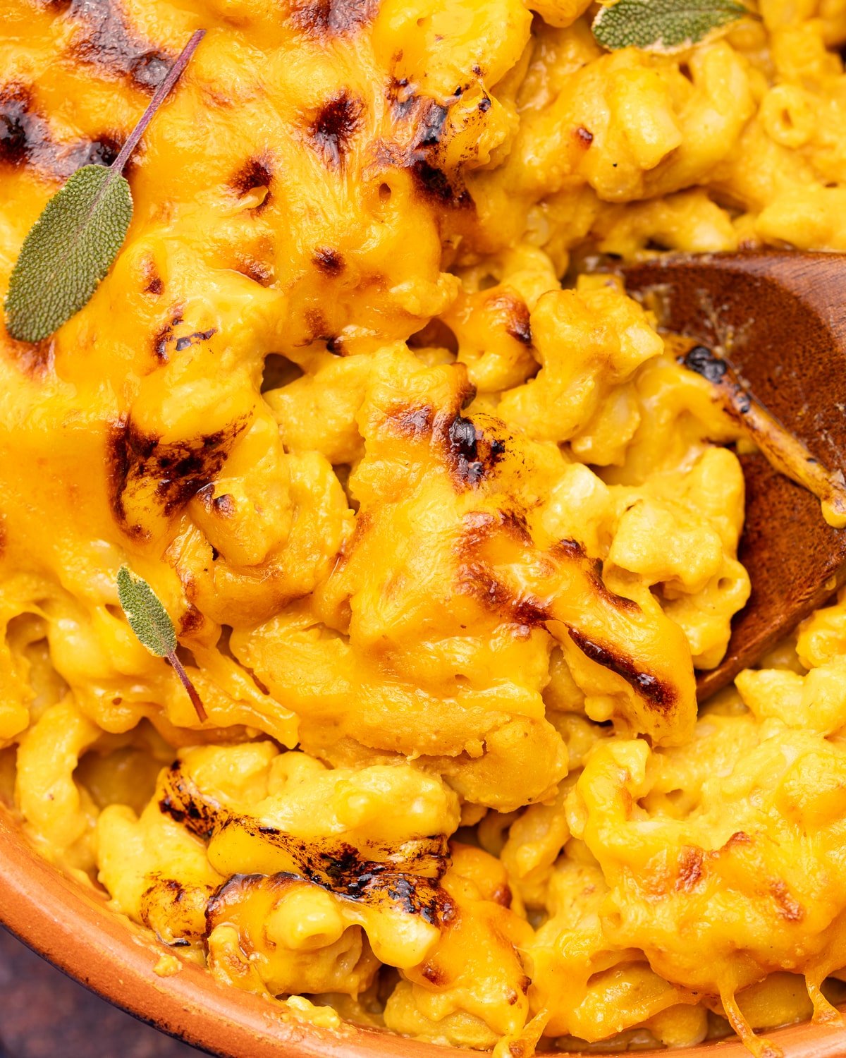 close up of cheesy, saucy vegan pumpkin mac and cheese with a wooden spoon. 