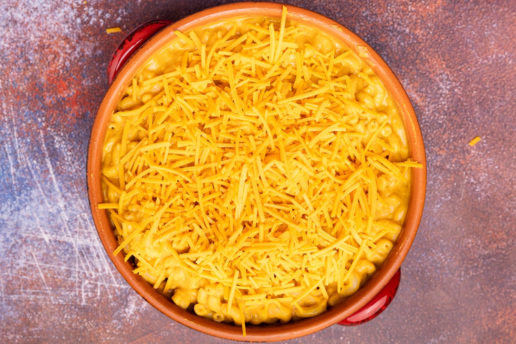 vegan pumpkin mac and cheese topped with shredded cheese before broiling