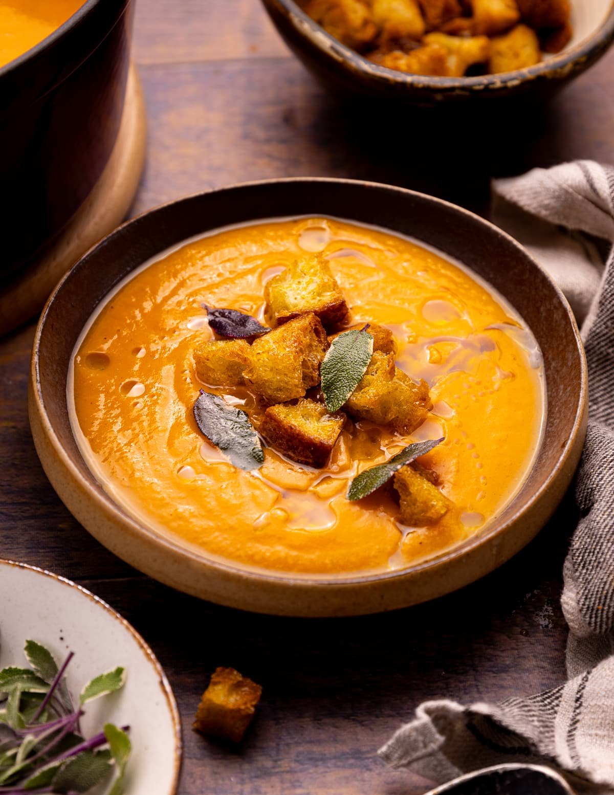 a bowl of sweet potato soup topped with golden croutons, a drizzle of olive oil and some fresh sage leaves. 