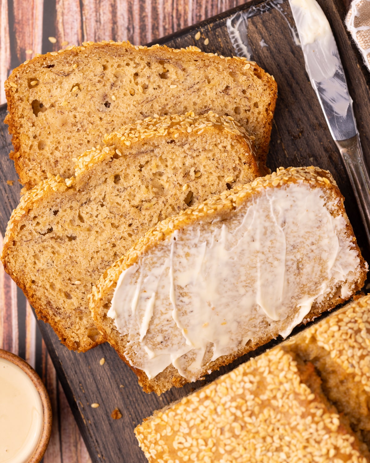 3 slices of tahini banana bread on a wooden board. One is buttered. 