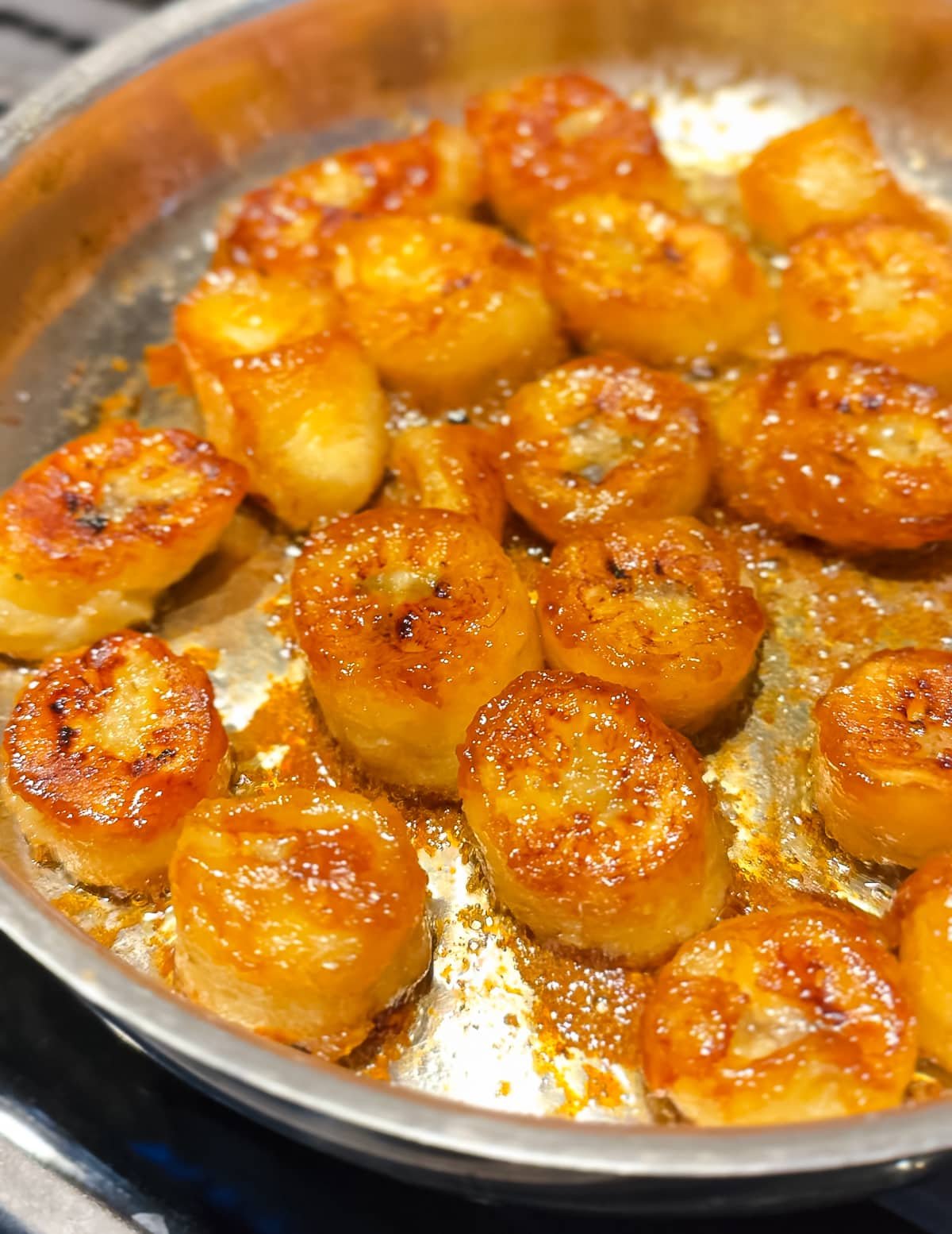 a stainless steel pan full of golden, sticky, vegan caramelized bananas