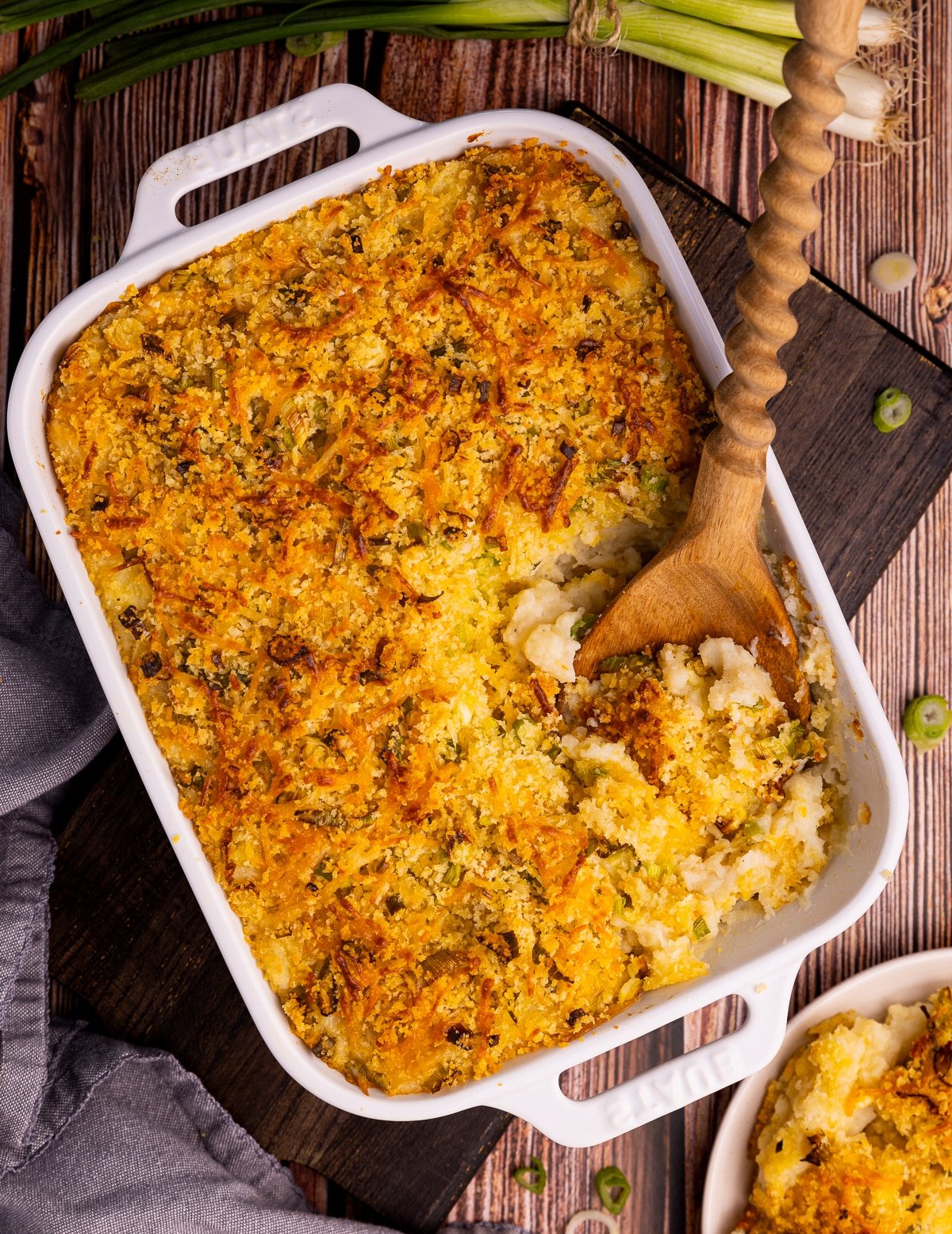 Mashed potato casserole in a white Staub dish with a corner cut out and a wooden spoon still in it. 