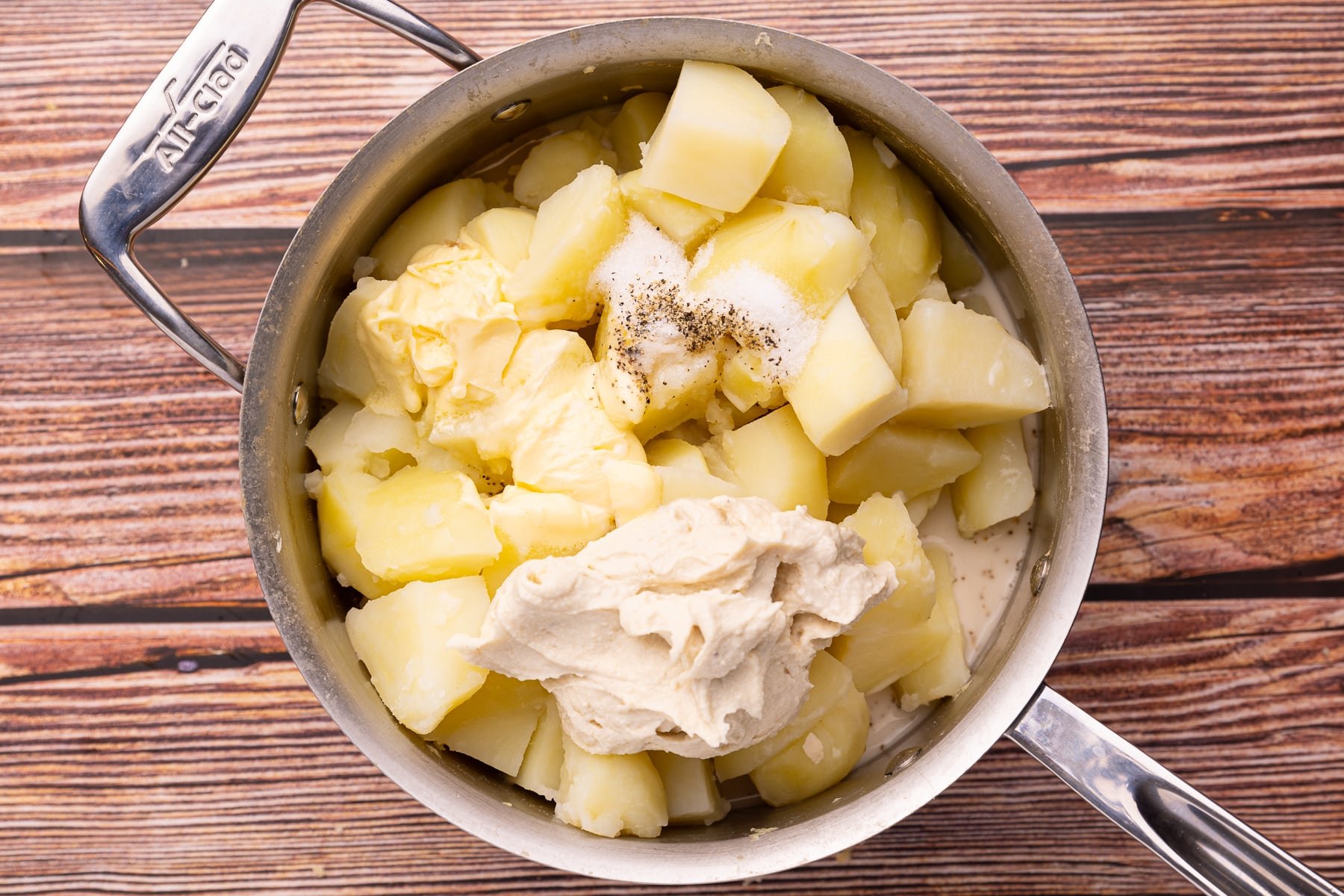 a saucepan with boiled potatoes, a dollop of cream cheese, melty butter, salt and pepper. 