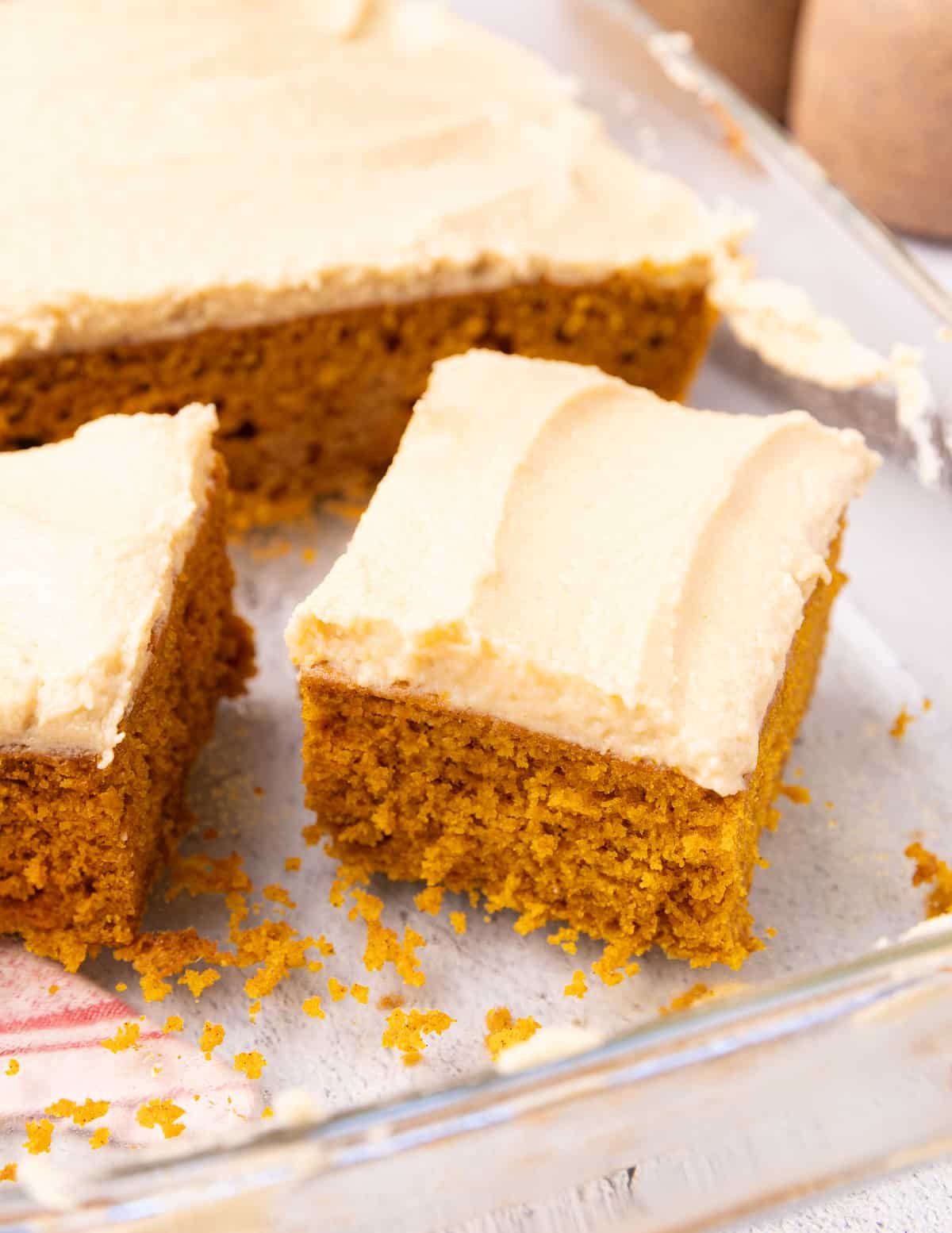 a square of vegan pumpkin cake with brown sugar frosting in a glass baking dish