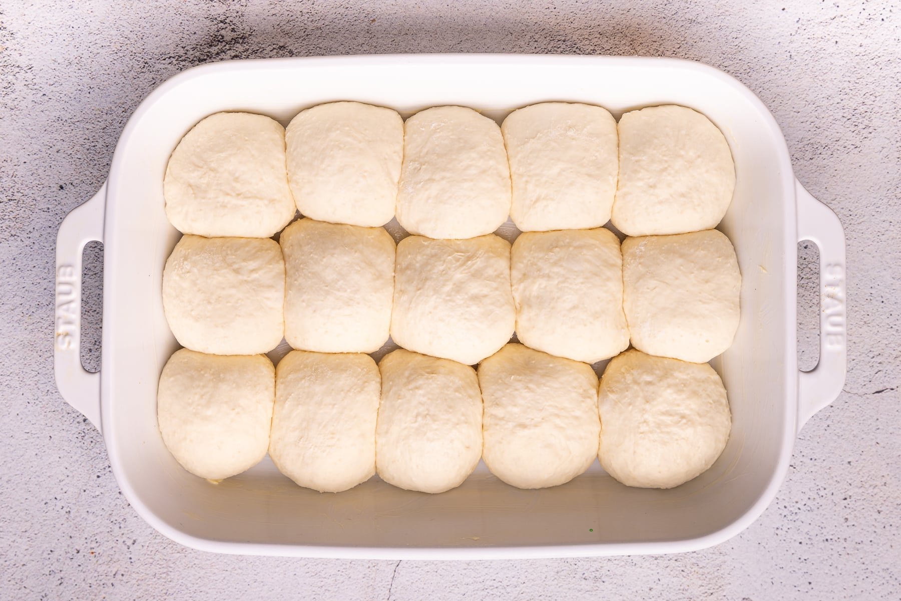 risen but uncooked dinner rolls in a ceramic baking dish