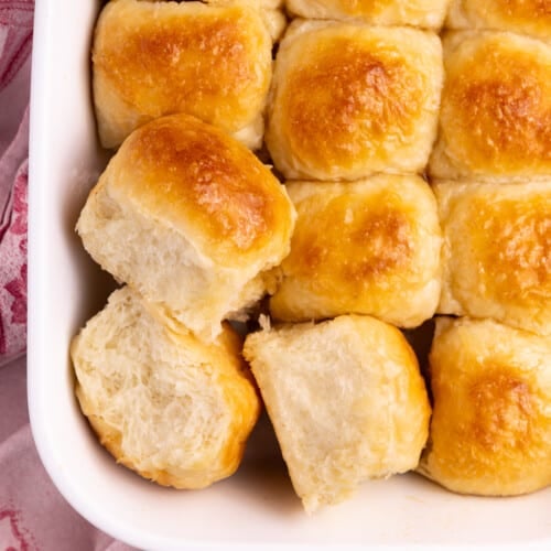 A dish of fluffy golden vegan dinner rolls from above. 3 rolls are turned to the side so you can see their fluffy sides.