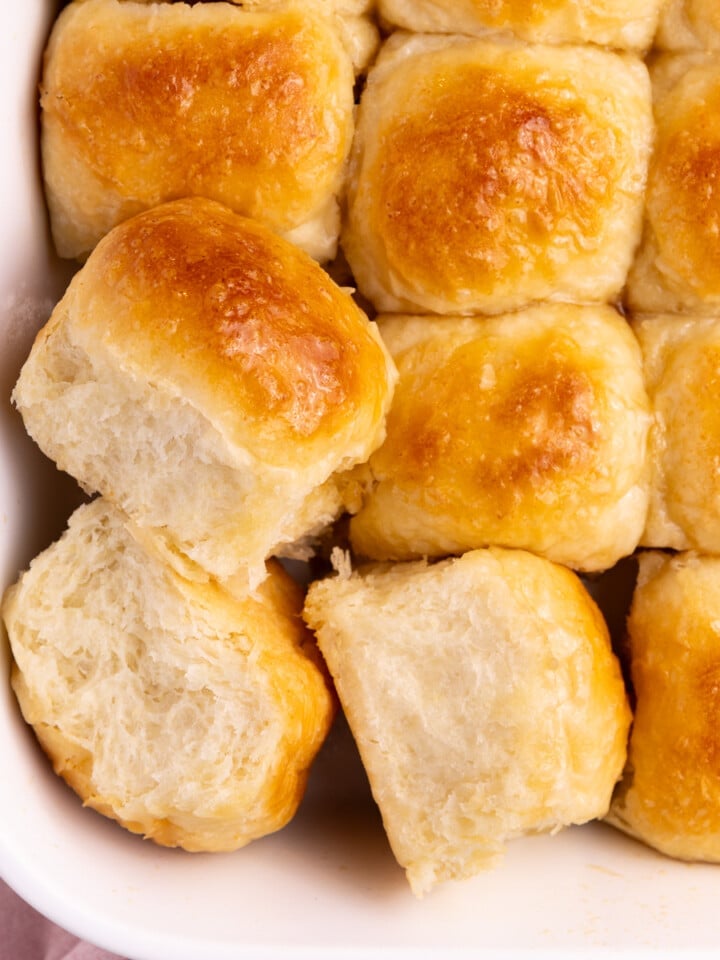 A dish of fluffy golden vegan dinner rolls from above. 3 rolls are turned to the side so you can see their fluffy sides.