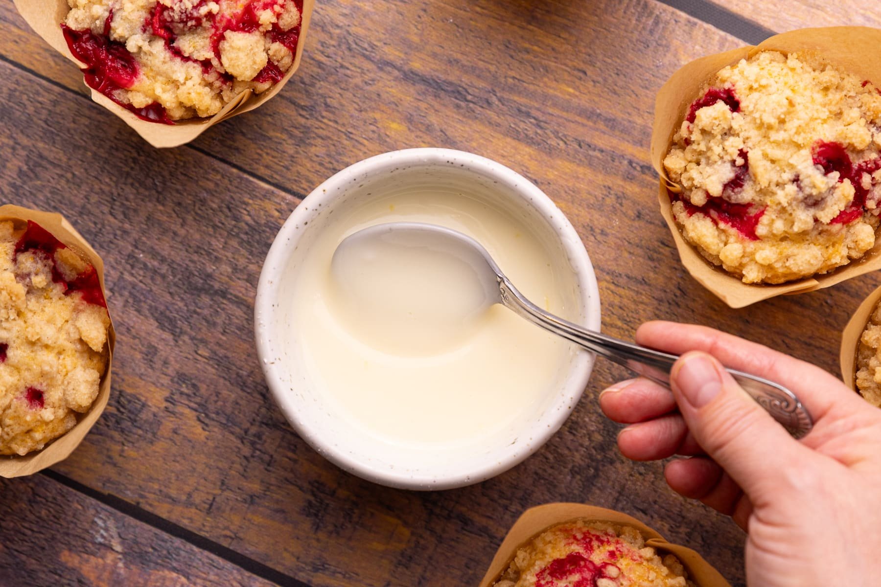 orange icing in a bowl surrounded by muffins