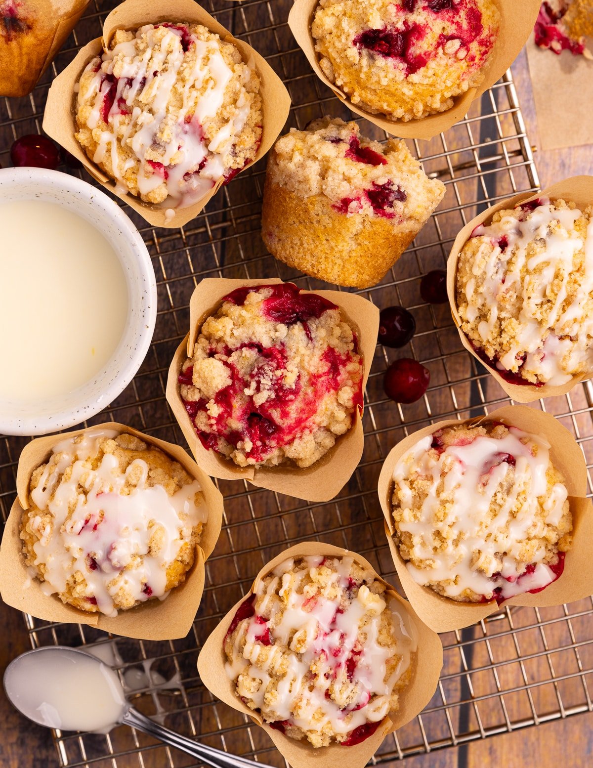 Vegan cranberry orange muffins on a wire rack. Some with drizzles of icing. 