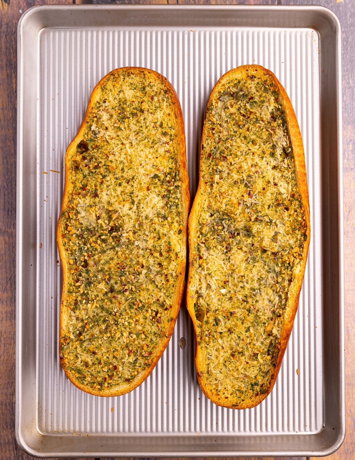 2 large pieces of golden, toasty looking garlic bread on a baking tray.