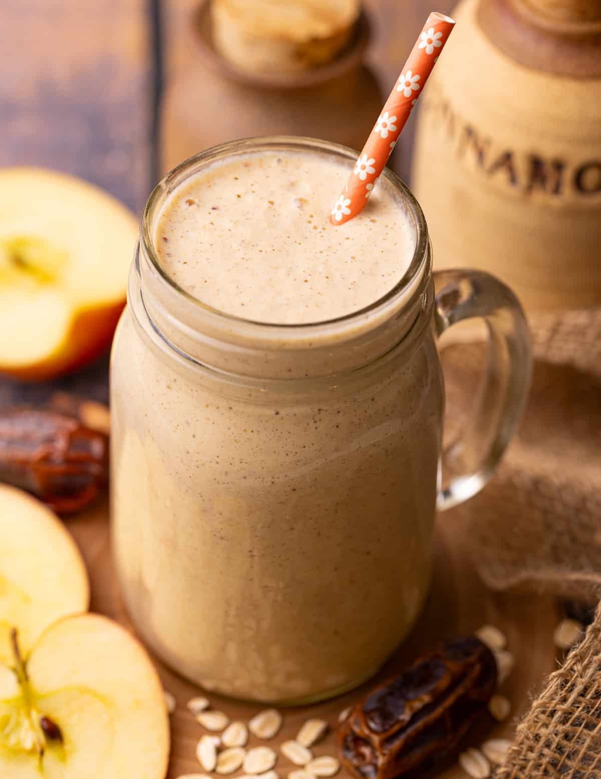 Apple oatmeal smoothie in a mason jar style glass with an orange paper straw. 