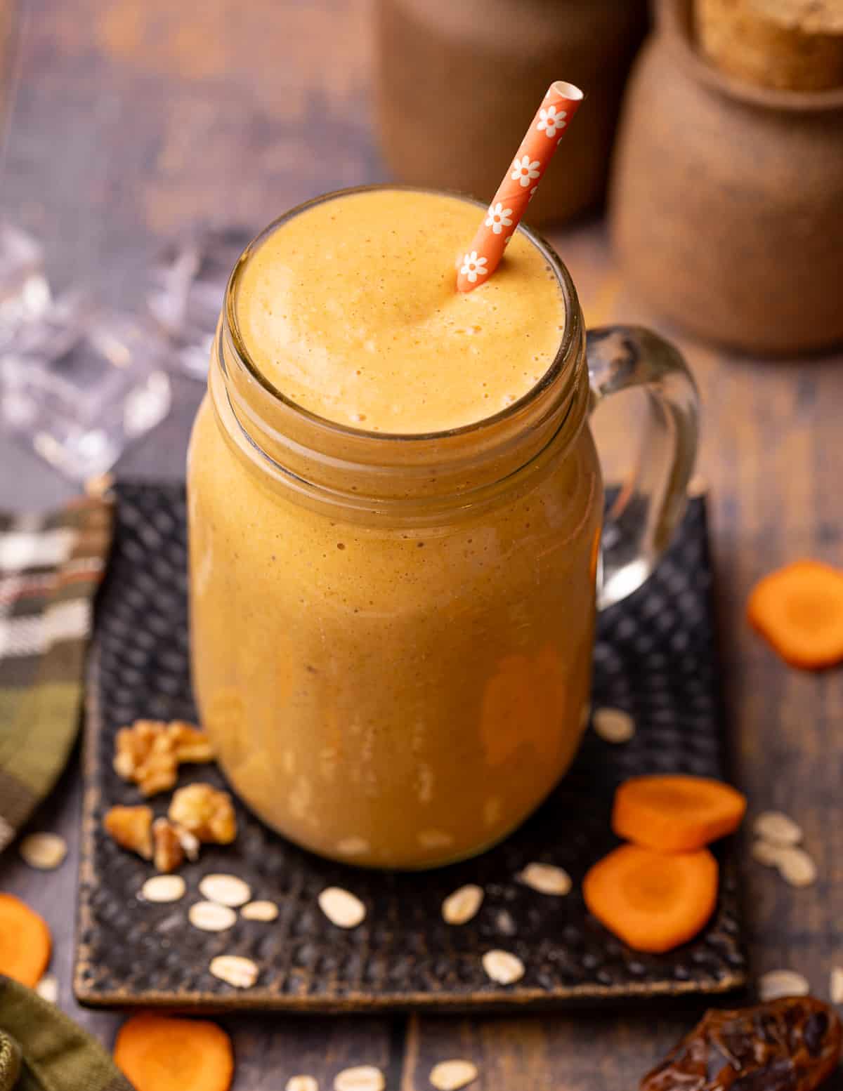 A glass of carrot cake smoothie with an orange flowery straw. 