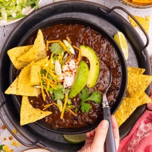 a bowl of Instant Pot Black bean soup with toppings like tortilla chips, avocado, green onion, vegan sour cream and cheese.