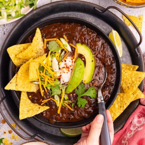 a bowl of Instant Pot Black bean soup with toppings like tortilla chips, avocado, green onion, vegan sour cream and cheese.