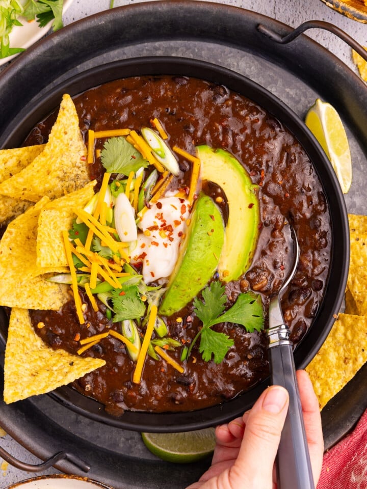 a bowl of Instant Pot Black bean soup with toppings like tortilla chips, avocado, green onion, vegan sour cream and cheese.