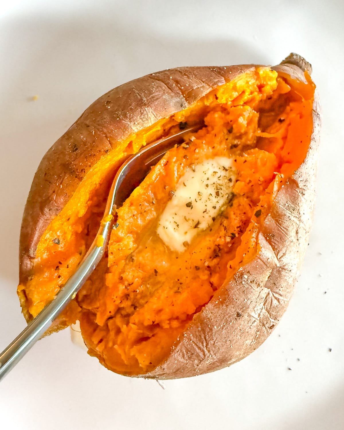 a split cooked sweet potato with vegan butter and black pepper.