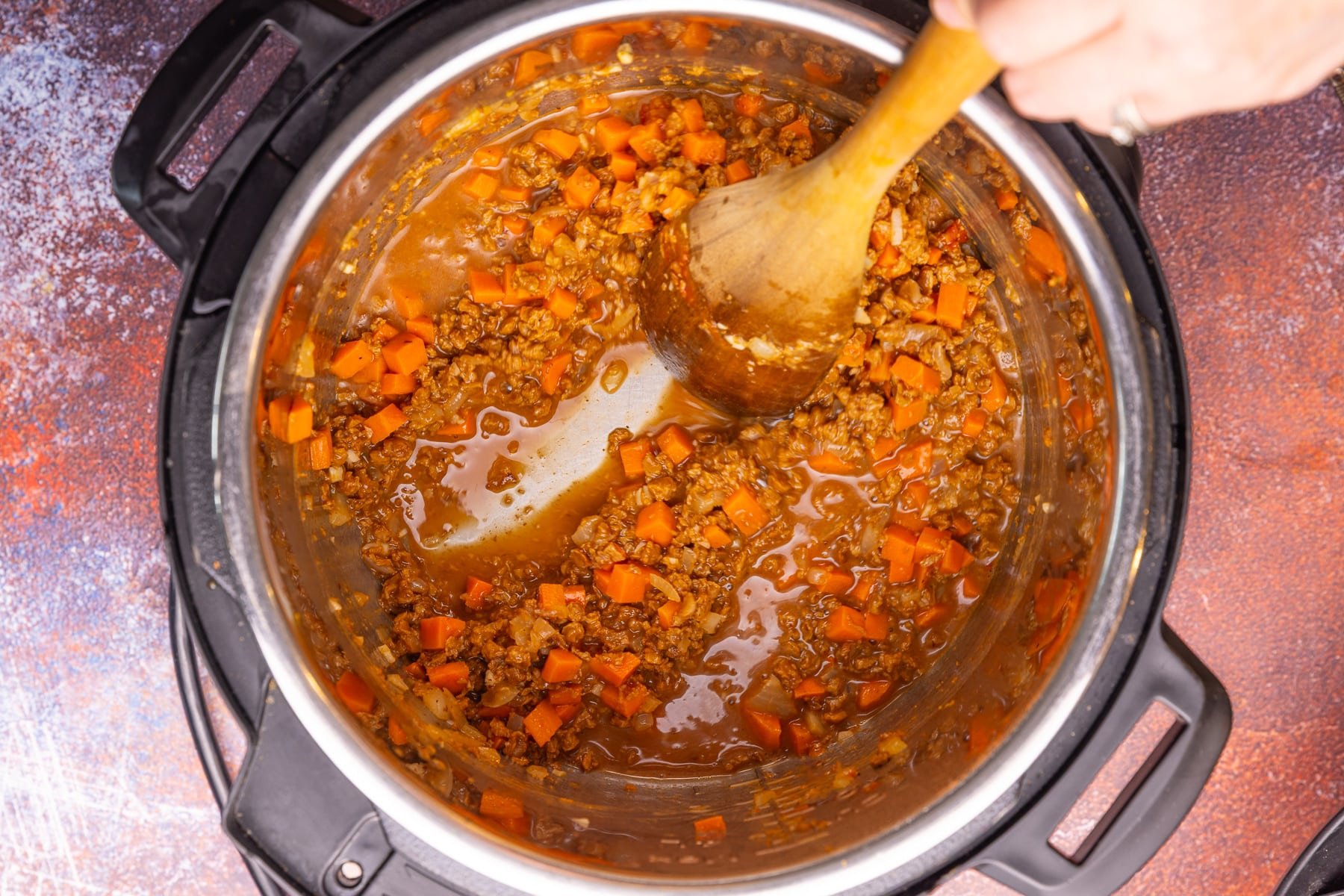 scraping the bottom of the Instant Pot bowl clean with a wooden spoon