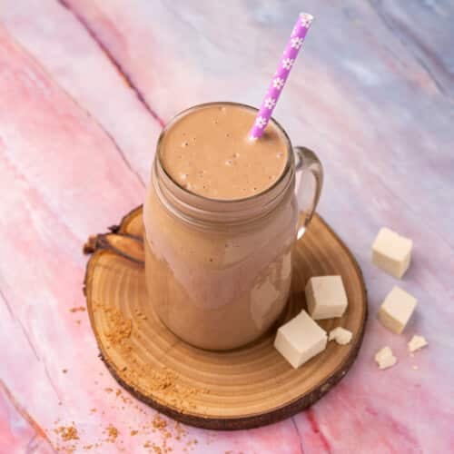 a chocolatey tofu smoothie in a glass with a flowery purple straw