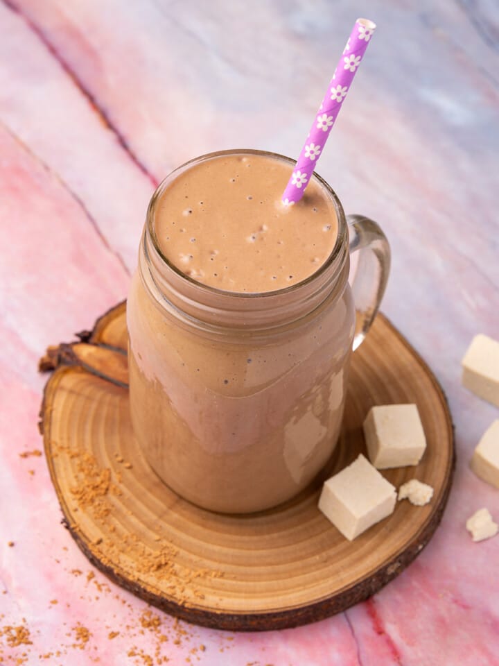 a chocolatey tofu smoothie in a glass with a flowery purple straw