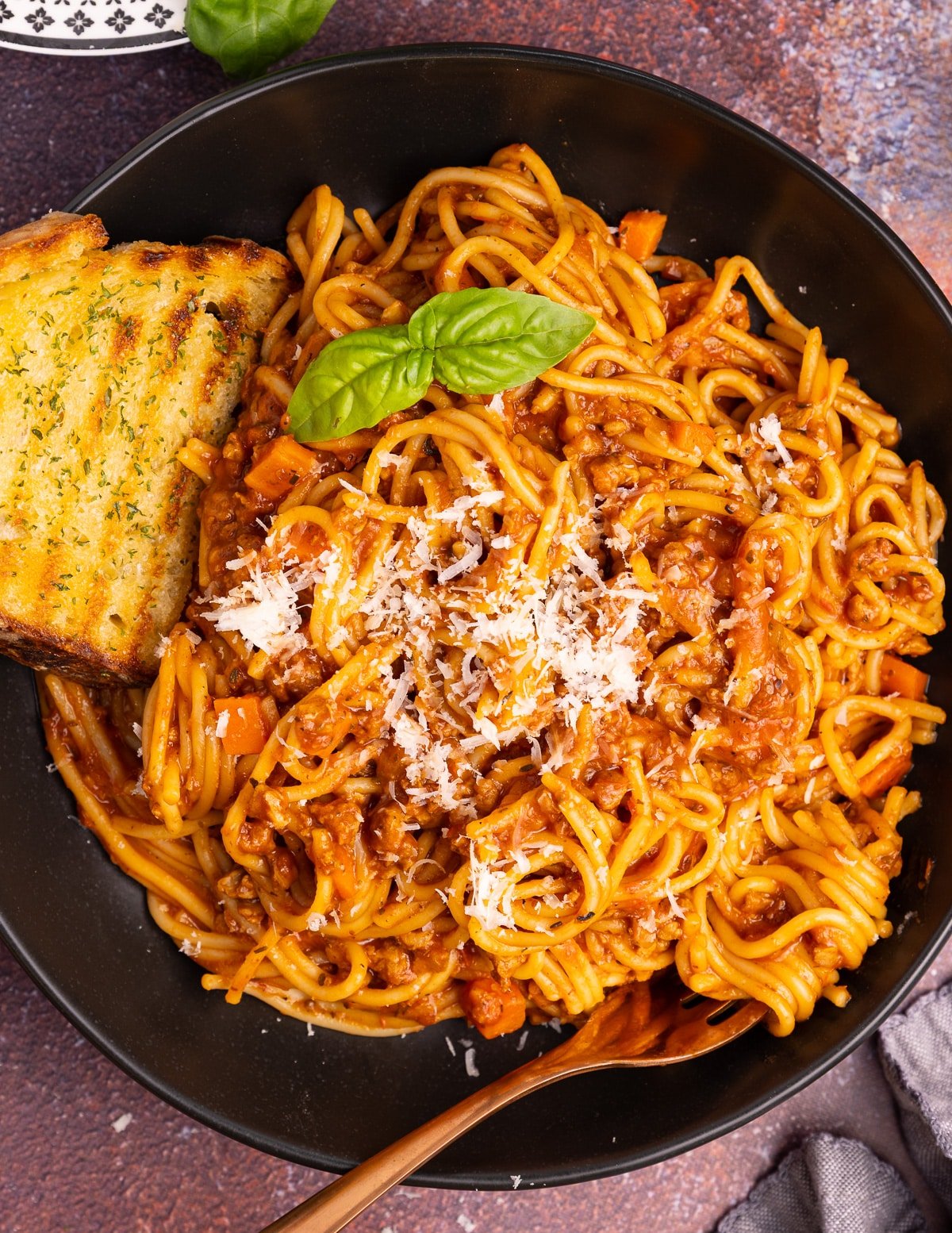 spaghetti bolognese on a plate with a piece of garlic toast.