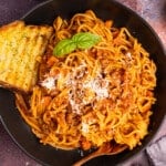 vegan spaghetti bolognese on a plate with a piece of garlic toast