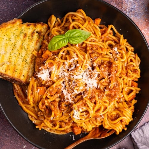 vegan spaghetti bolognese on a plate with a piece of garlic toast