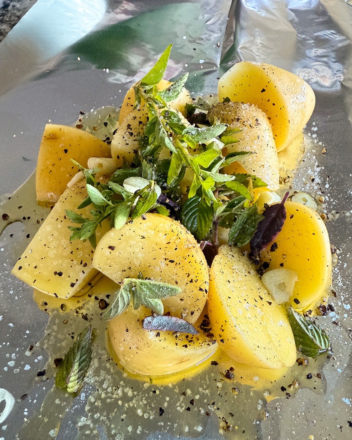 uncooked grilled potatoes, herbs, and seasonings in foil
