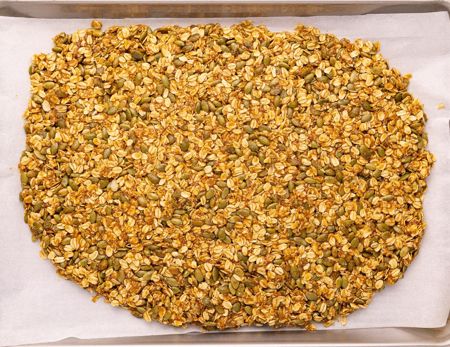uncooked granola spread out on a baking tray