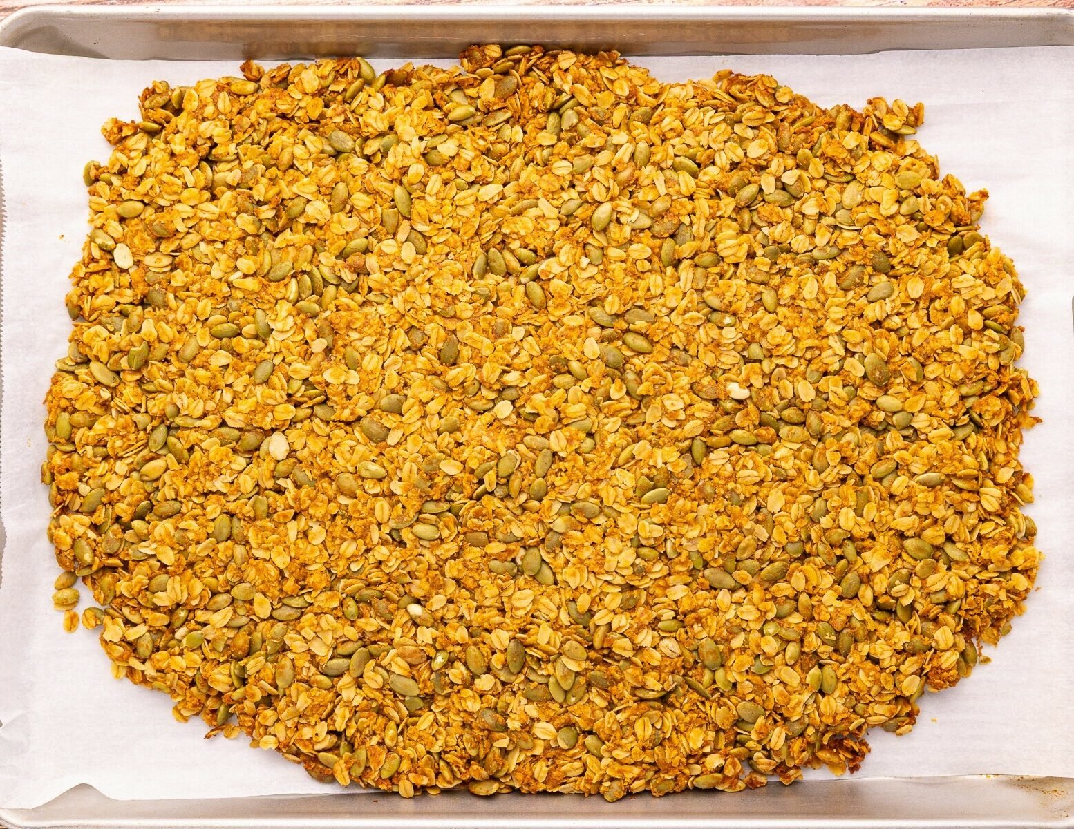 cooked granola spread out on a baking tray prior to being broken into pieces