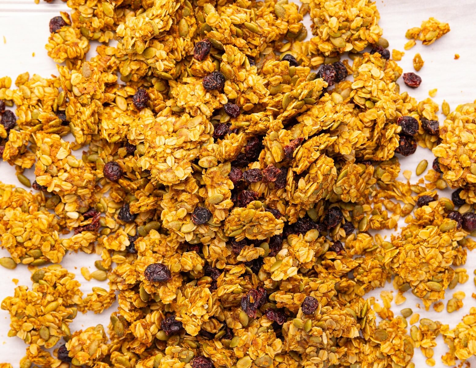 clumpy pieces of pumpkin seed granola and dried cranberries on a baking tray