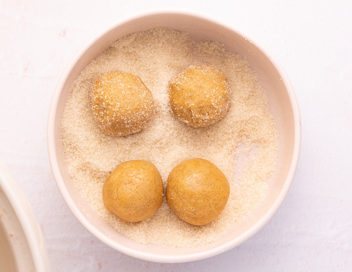 cookie dough balls in a bowl of granulated sugar