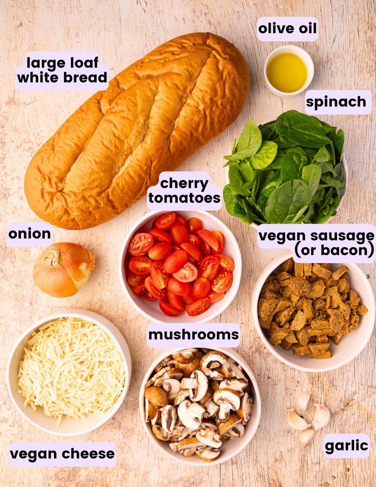 bread, olive oil, spinach, onion, cherry tomatoes, vegan sausage, vegan cheese, mushrooms, and garlic.