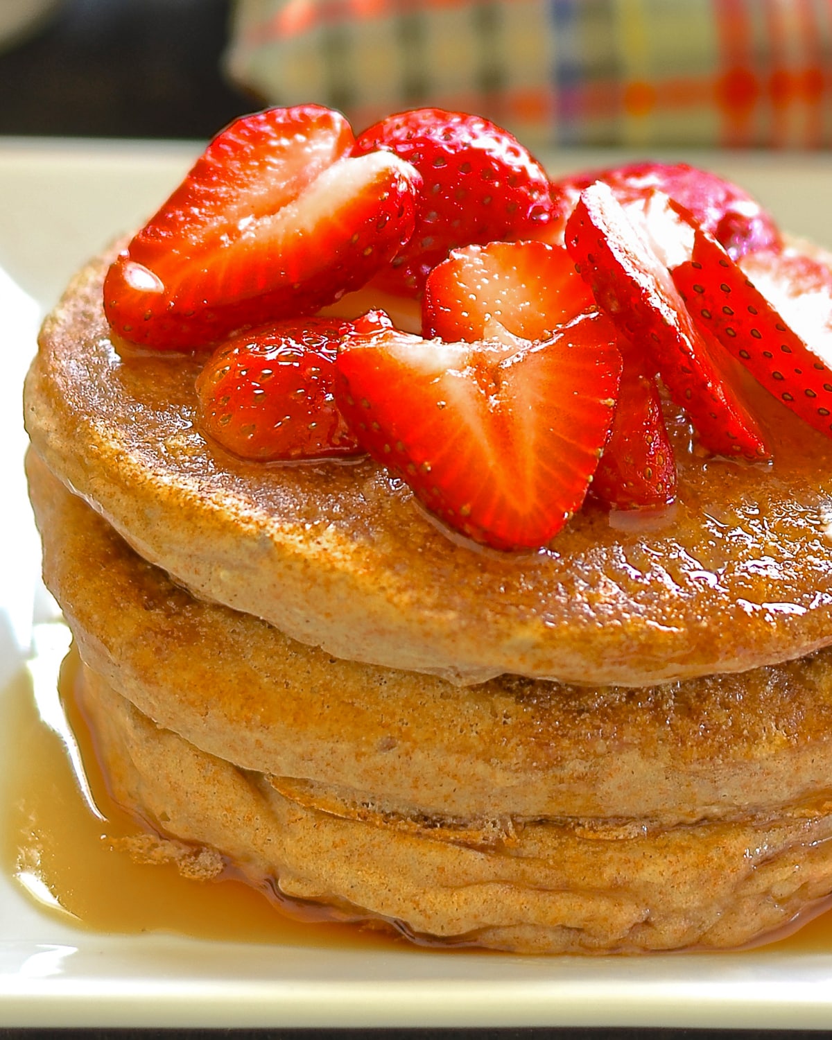 a stack of healthy vegan pancakes with strawberries and maple syrup