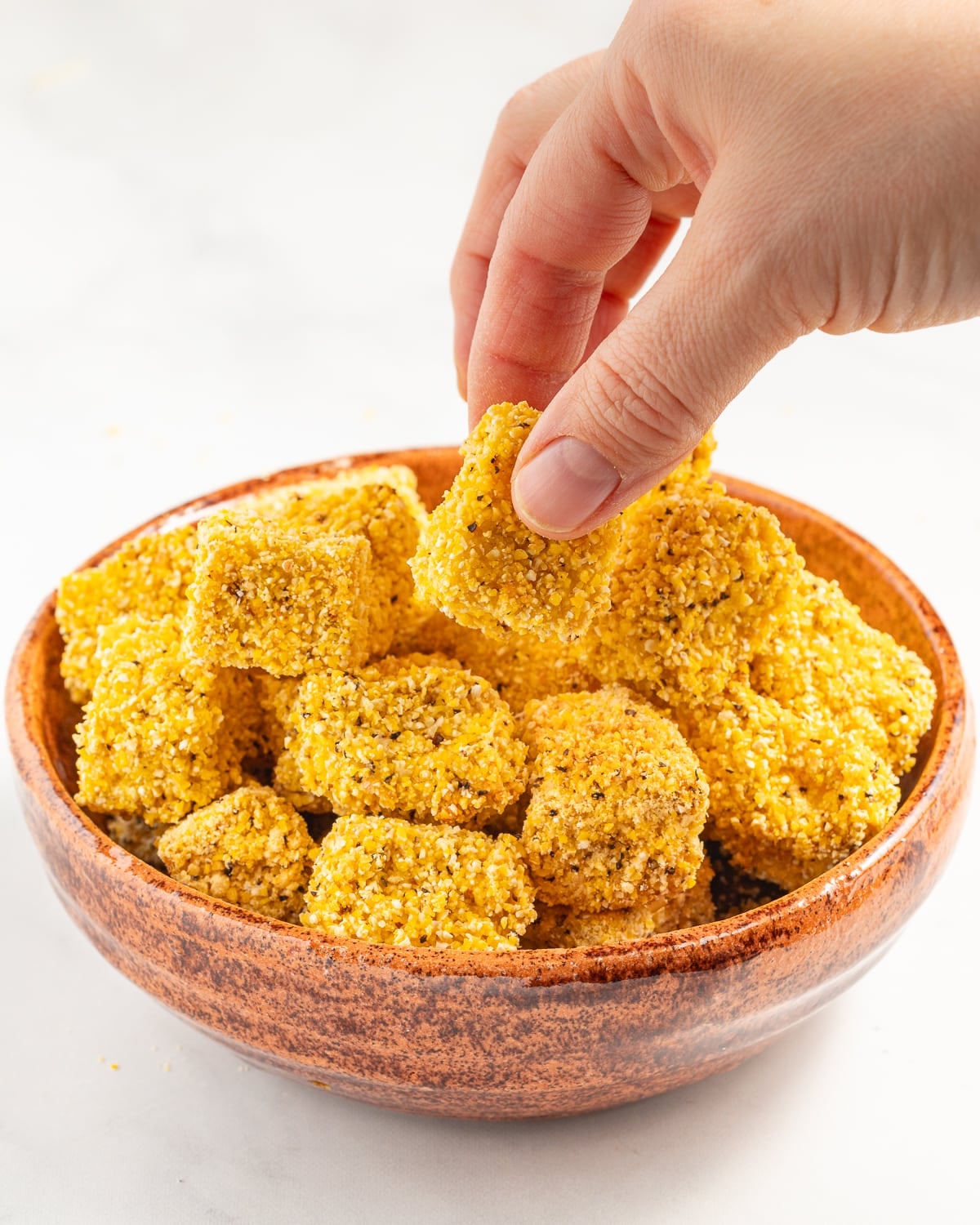a  hand taking a cube of tofu from a bowl